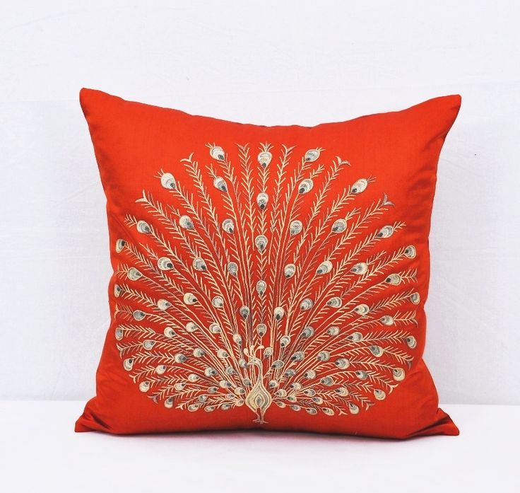 a red pillow with a gold embroidered peacock design on the front and back, sitting on a white surface