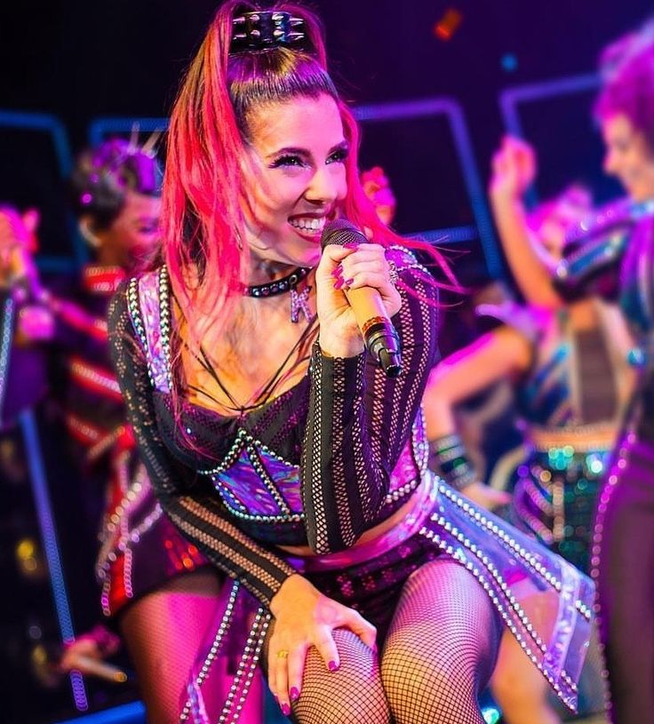 a woman with pink hair sitting on a stool in front of other women and dancers