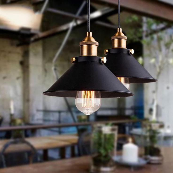 two black and gold pendant lights hanging over a wooden table with chairs in the background