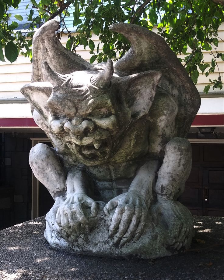 a stone gargoyle statue sitting on top of a cement slab next to a tree