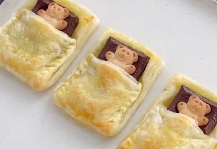 there are three small pastries with teddy bears in them on the plate and one has been cut into smaller squares