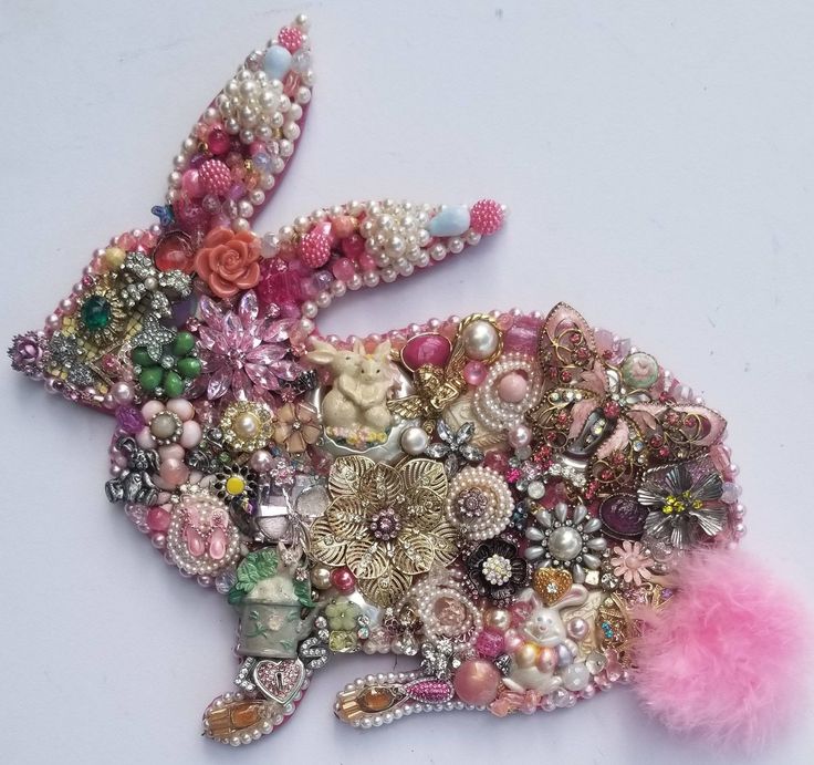 a rabbit made out of beads and other items on a white surface with pink feathers