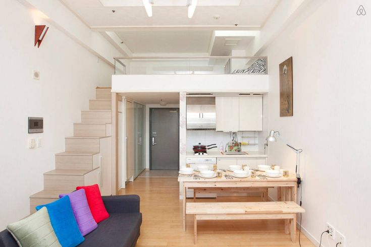 a living room filled with furniture next to a kitchen and stairway leading up to a loft