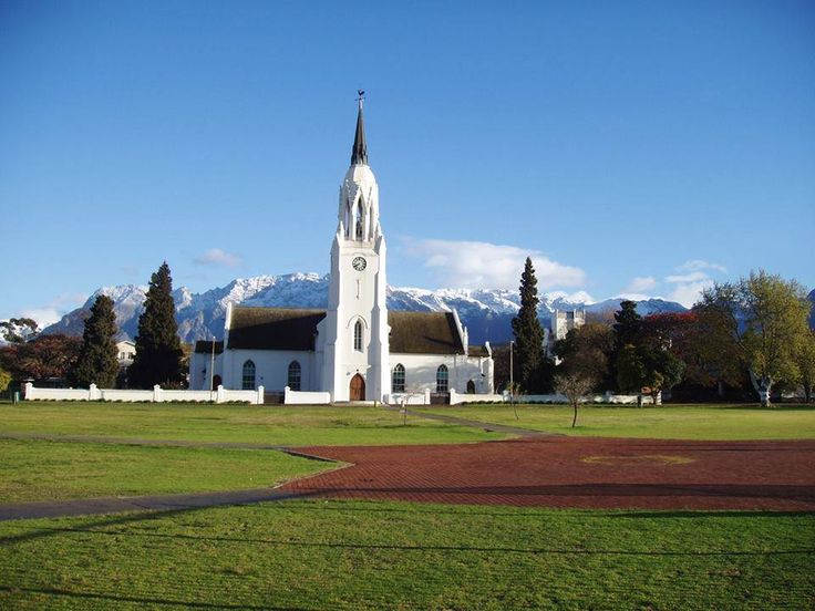 a large white church with a steeple on it's side and mountains in the background