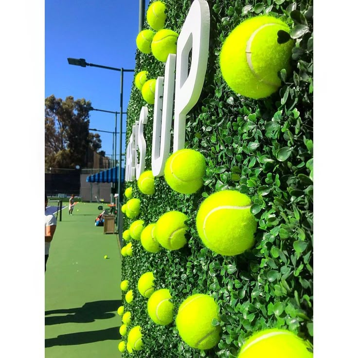 tennis balls are arranged on the side of a wall that is covered in artificial greenery