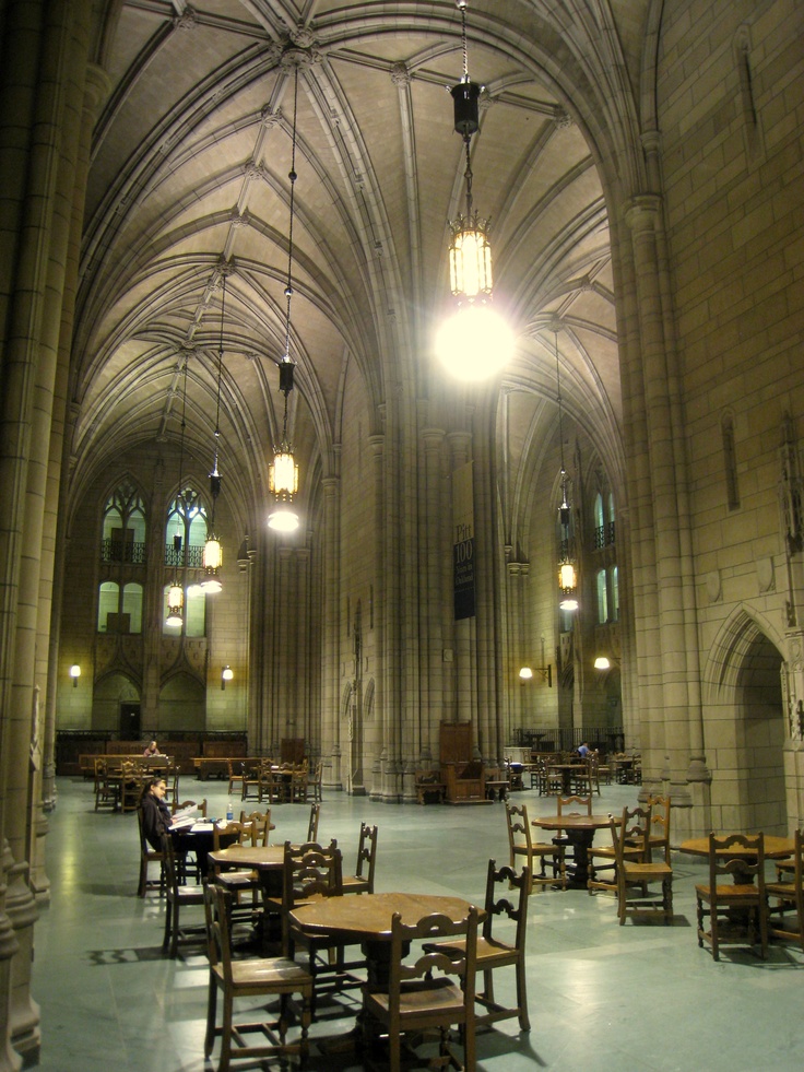 an empty dining hall with tables and chairs in the foreground is lit by two large chandeliers