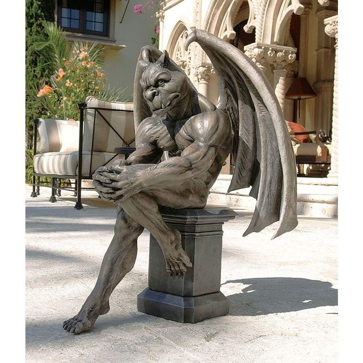 a statue of a gargoyle sitting on top of a pillar in front of a building