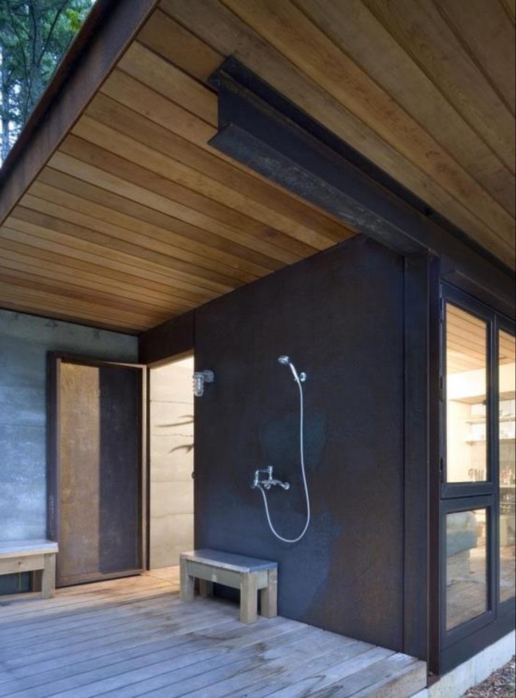 an outdoor shower on the side of a wooden deck next to a building with glass doors