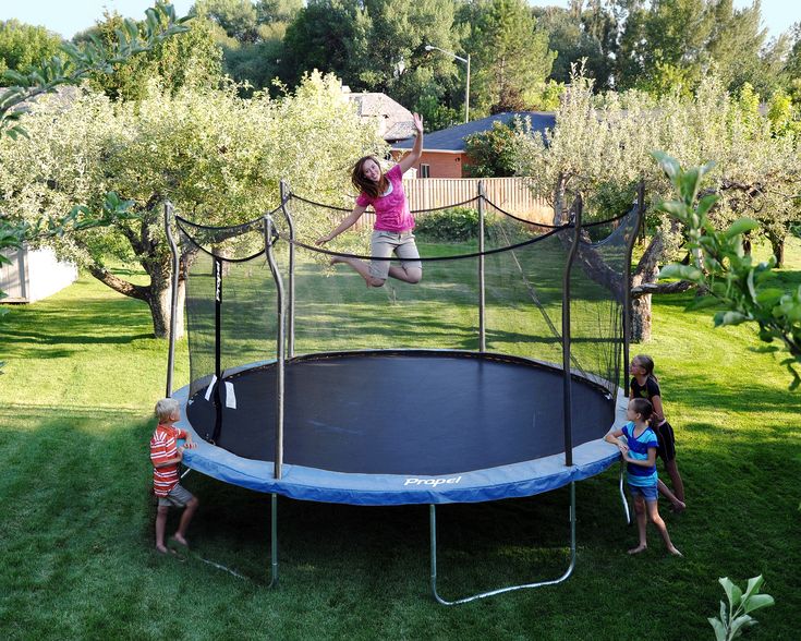 two children are playing on a trampoline in the yard with an adult nearby