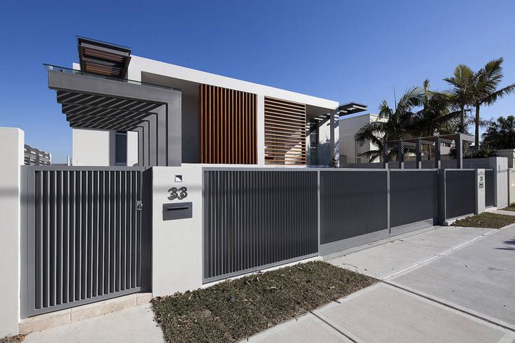 a modern house with an iron fence and wooden slats on the front door, along with palm trees