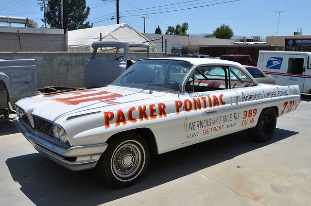 an old white police car parked in a parking lot next to other cars and trucks