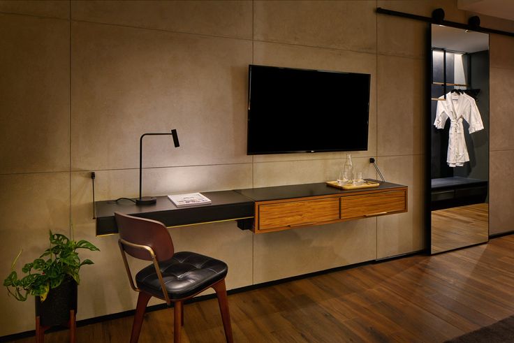 a room with a desk, chair and television on the wall next to a plant