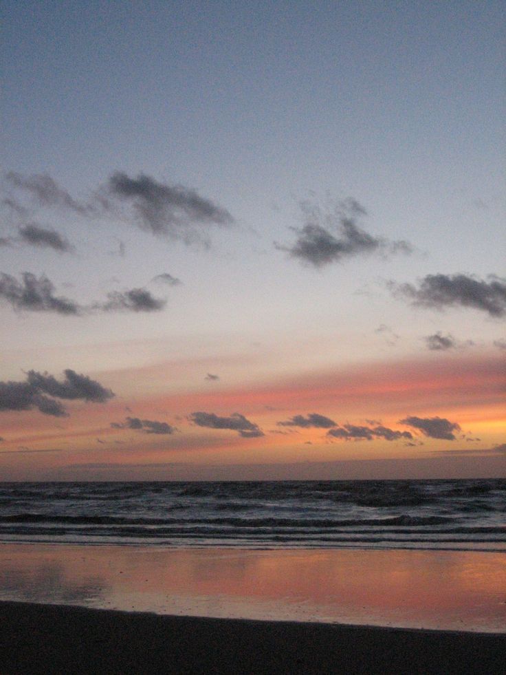 the sun is setting over the ocean and clouds are reflected in the wet sand on the beach