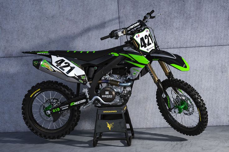 a green and black dirt bike sitting on top of a stand in front of a wall