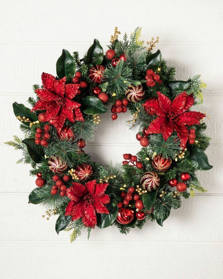 a christmas wreath with poinsettis and greenery hanging on a white wall