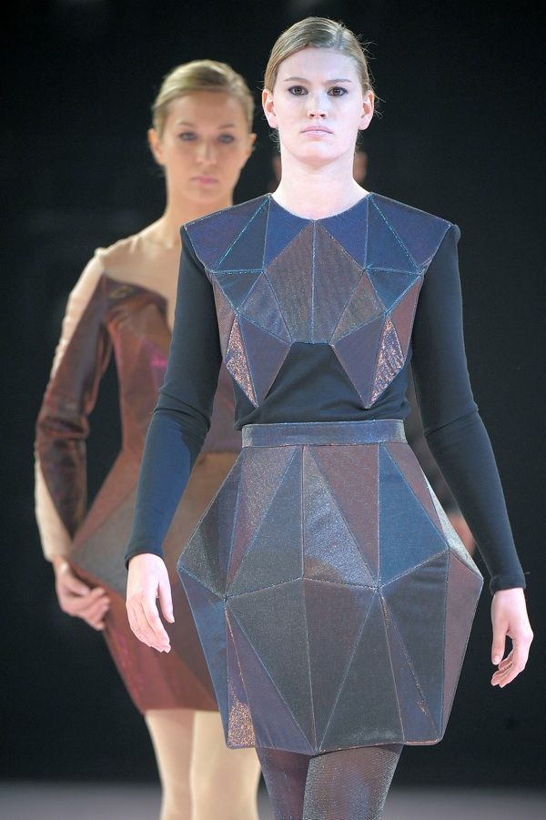 two women walking down the runway in dresses made out of geometrically shaped materials