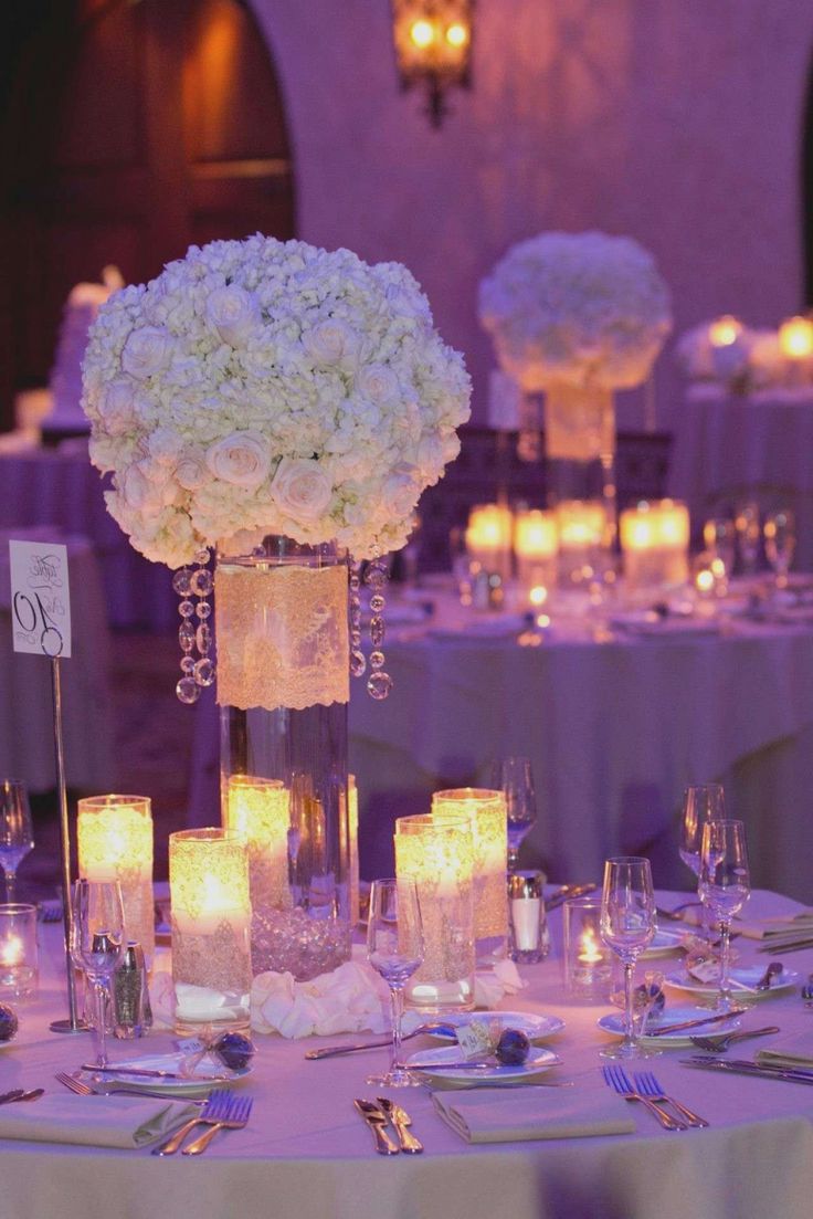 the centerpieces are filled with white flowers and lit candles for an elegant touch