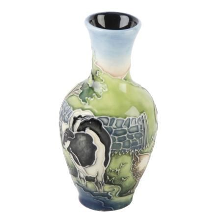 a black and white cow standing next to a green vase