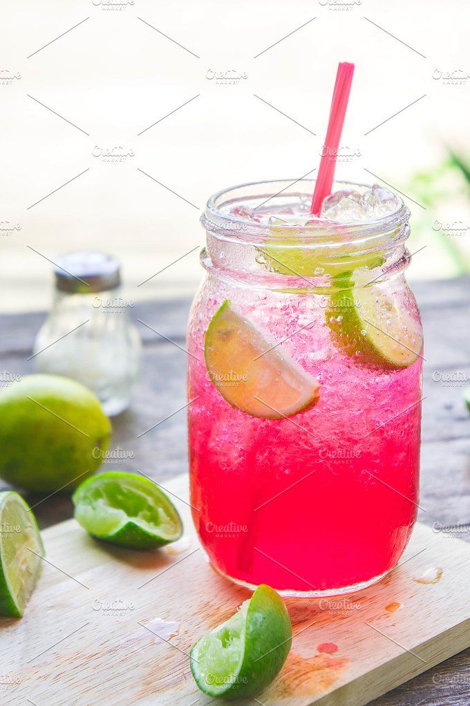 a pink lemonade drink with limes and ice on a cutting board next to it