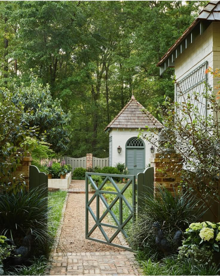 a brick path leads to a small white building in the middle of trees and shrubs