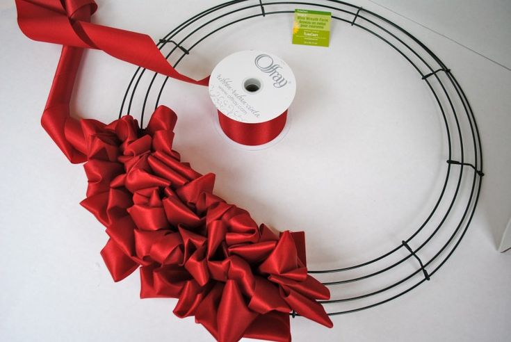 a red ribbon is tied on a wire wreath with a reel of thread next to it