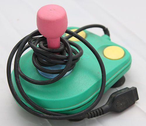 a green and pink game controller sitting on top of a white table next to a black cord