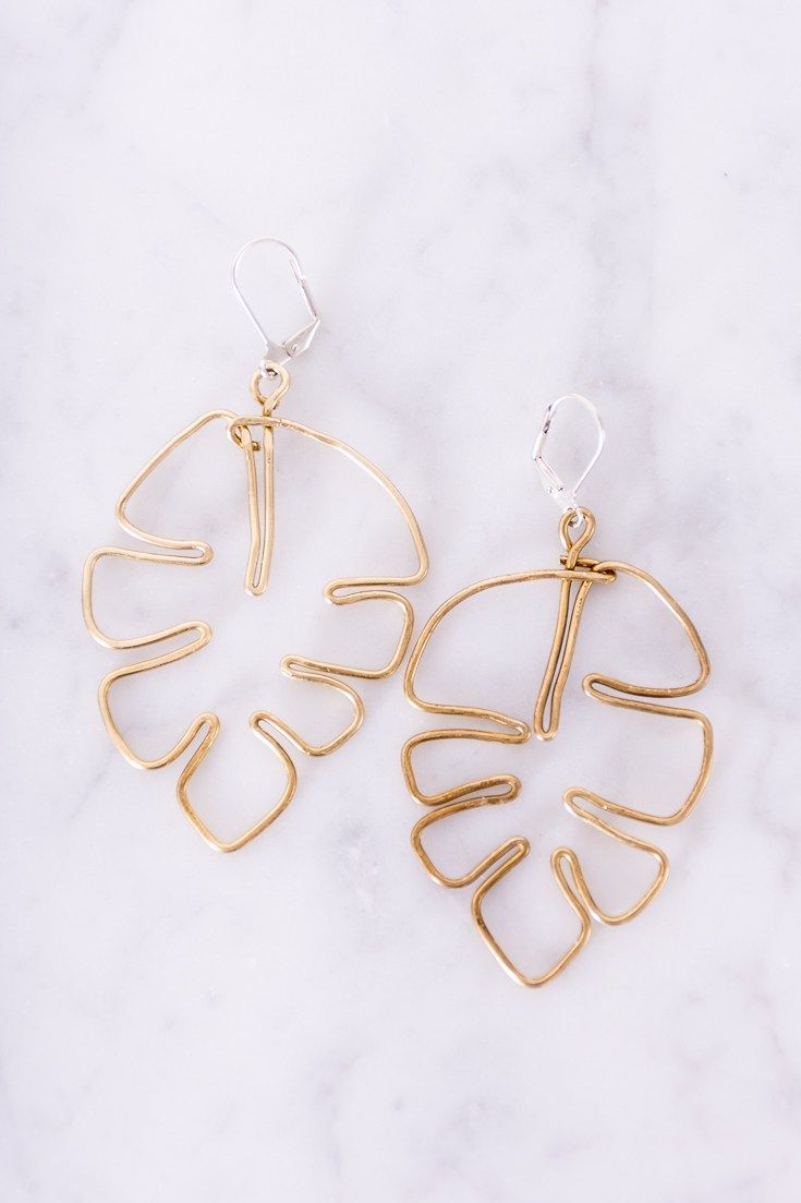 the large gold leaf earrings are on top of a marble countertop, with one earring