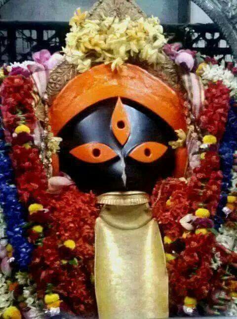 a statue with an orange and black mask on it's face, surrounded by flowers