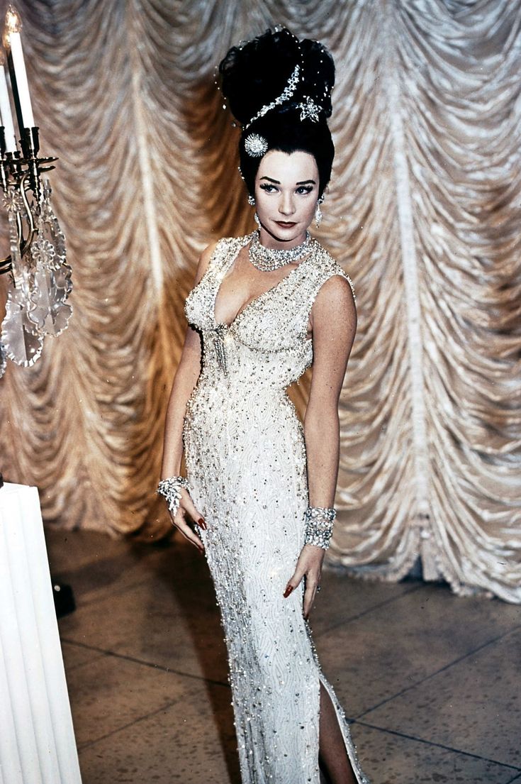 a woman in a white dress standing next to a chandelier