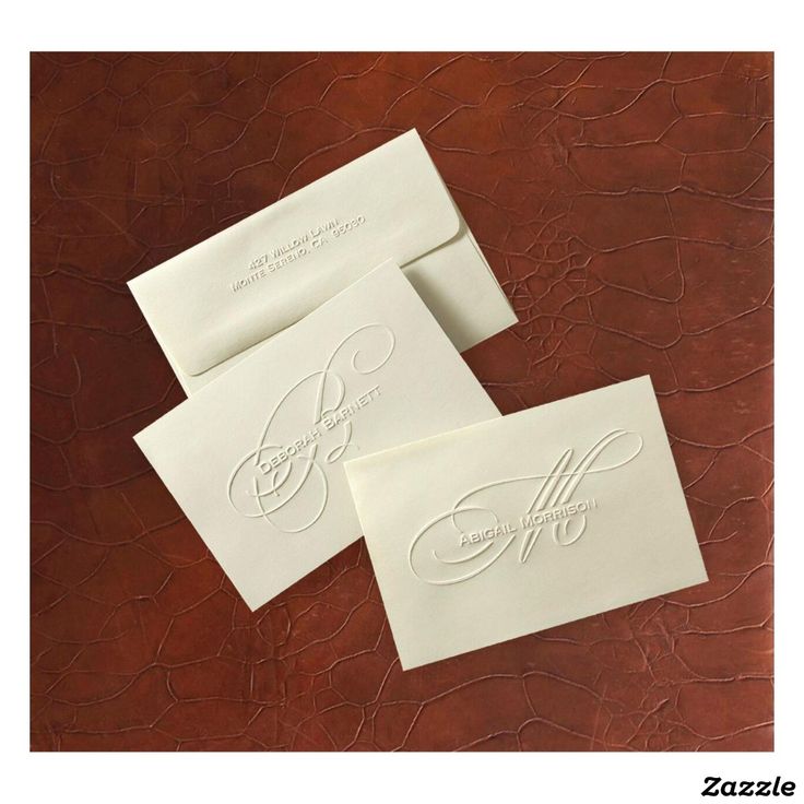 three white envelopes with monogrammed designs on them sitting on a brown leather surface