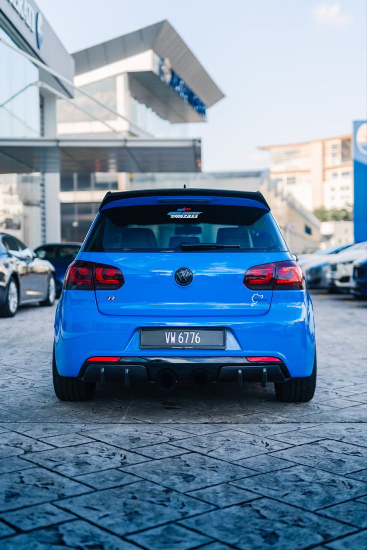 the back end of a blue car parked in front of a building with other cars