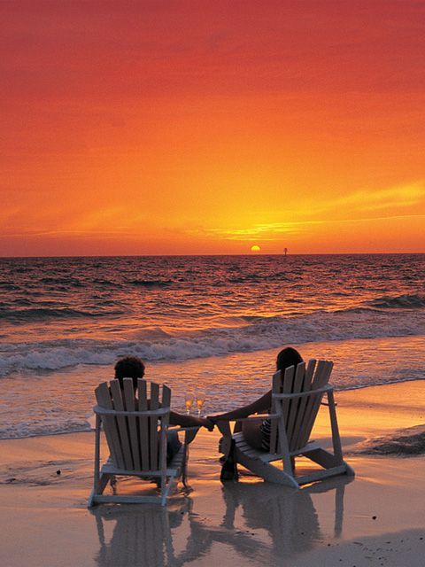 two people sitting in chairs on the beach watching the sun go down and have a beautiful evening