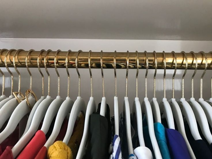 a rack with many different colored shirts hanging from it's hooks and gold handles