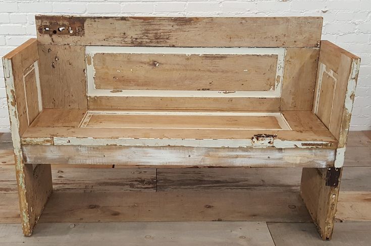 an old wooden bench sitting in front of a white brick wall