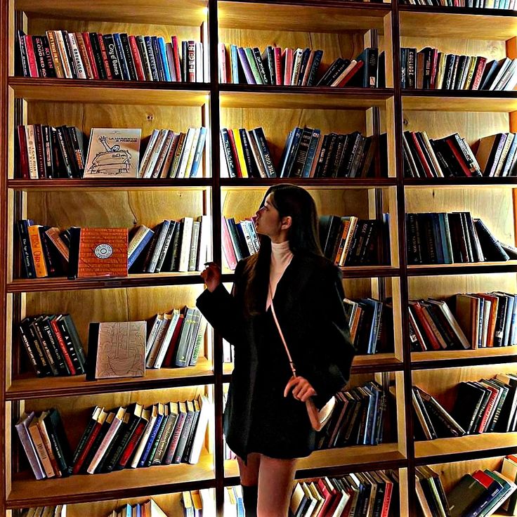 a woman standing in front of a book shelf filled with books