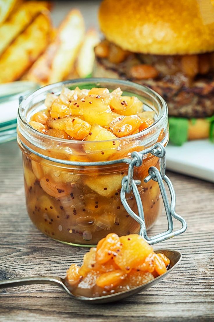 a jar filled with food sitting on top of a wooden table next to a burger