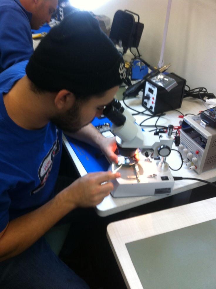 two men sitting at a table working on electronic equipment in front of a laptop computer