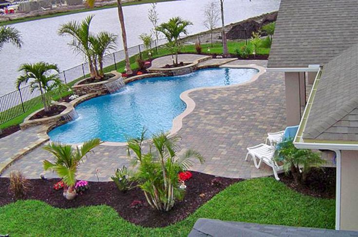 an outdoor swimming pool surrounded by lush green grass and palm trees next to a lake