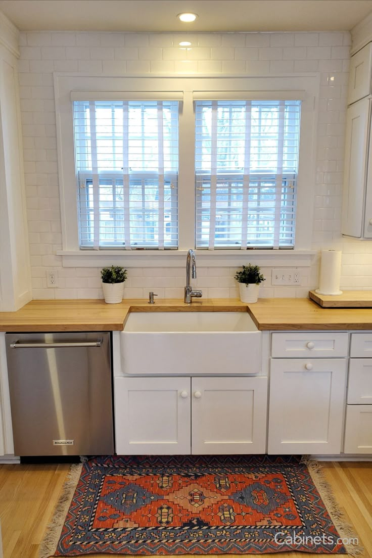 a kitchen with white cabinets and wooden counter tops, an area rug in front of the sink