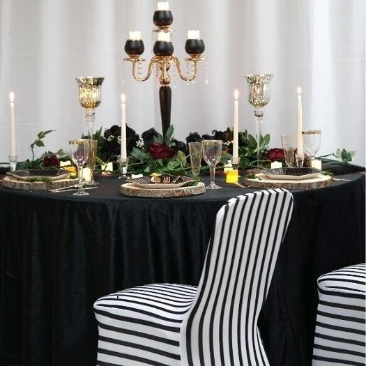 a table with black and white striped chairs, candles and greenery on ...