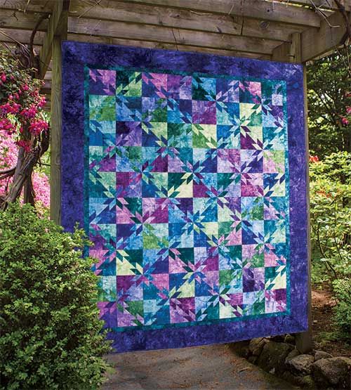 a blue and purple quilt hanging from a pergolated wooden structure in a garden