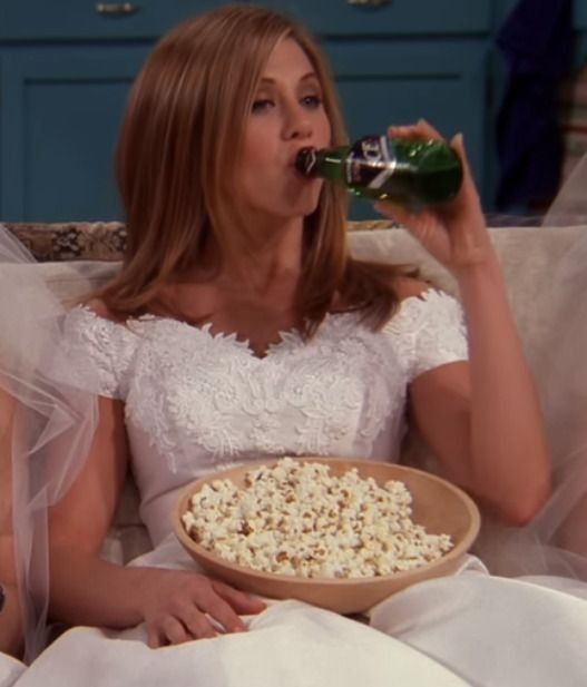 two women sitting on a couch eating popcorn and drinking beer while holding beers in their hands