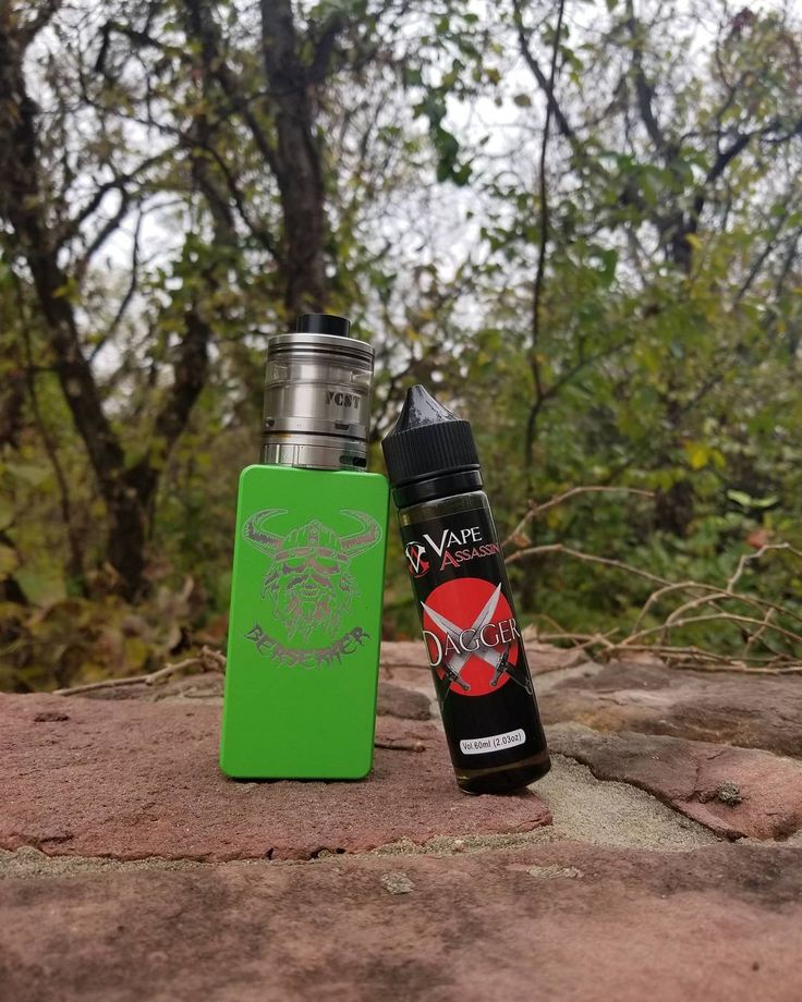 a green lighter next to an electronic device on top of a stone surface with trees in the background