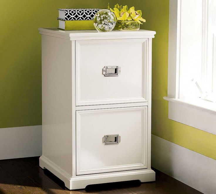 a white filing cabinet with two drawers in front of a green wall and wooden floor