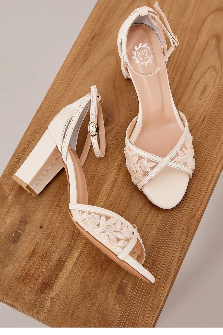 a pair of white high heeled shoes sitting on top of a wooden table next to a shoe box