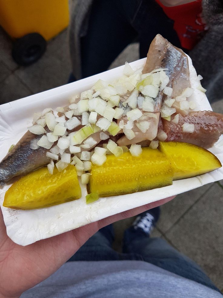 a person holding up a paper plate with some food on it and fish in it