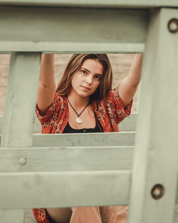 a young woman sitting on top of a wooden bench with her hands in the air