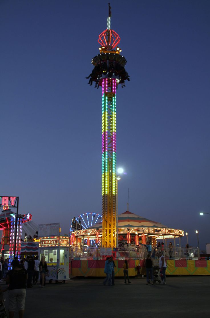 people are standing around in front of a carnival ride at night with the ferris wheel lit up