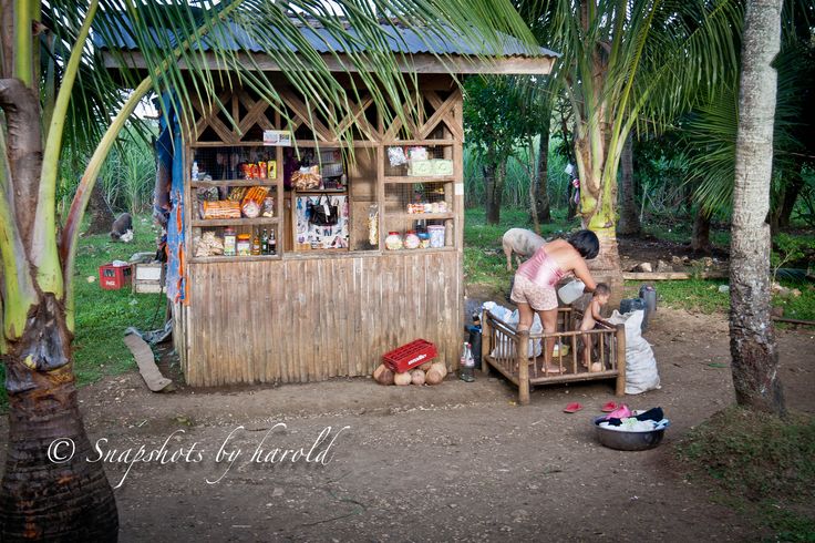 a man sitting on a bench in front of a small hut with a wooden roof