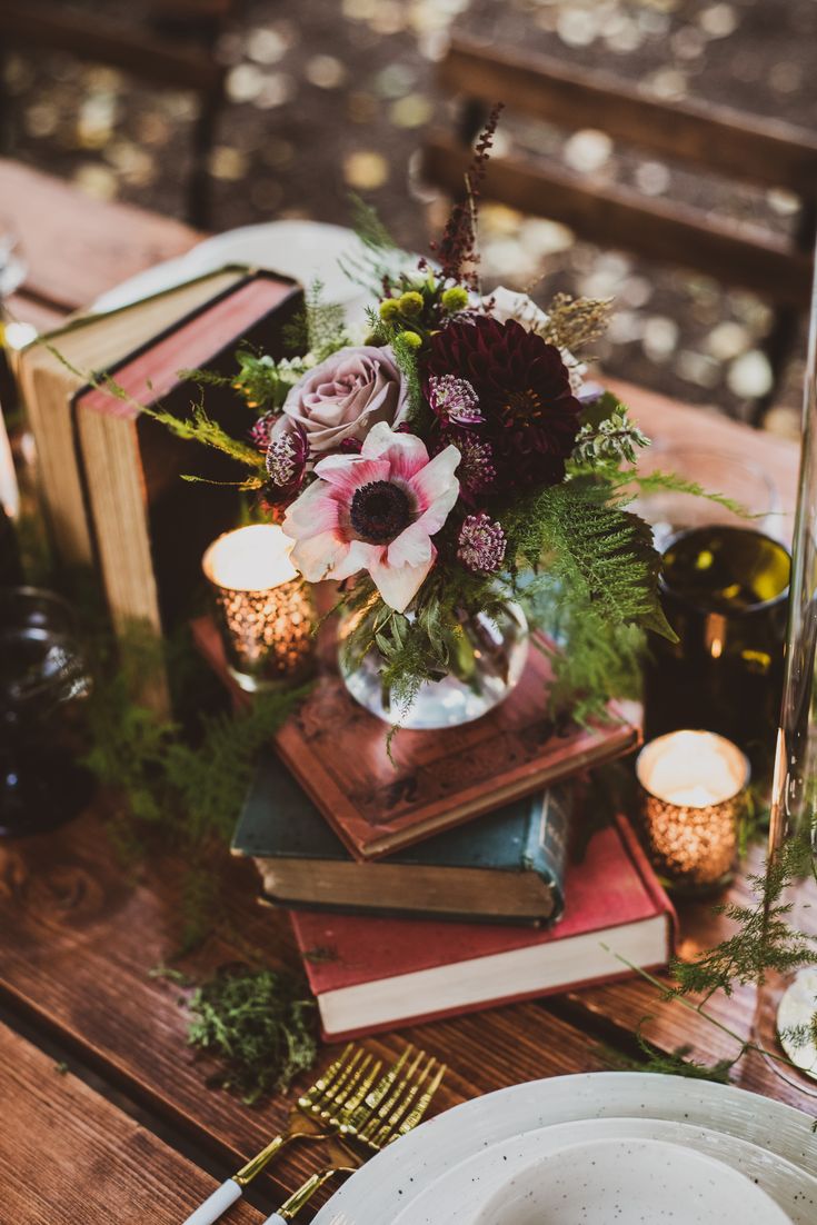 a table topped with books and flowers on top of a wooden table next to candles